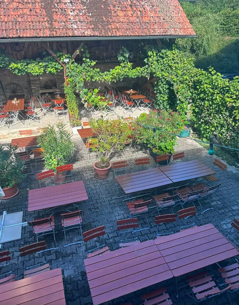 Blick von oben in den Innenhof mit Tischen, Blumen und Weinlaub