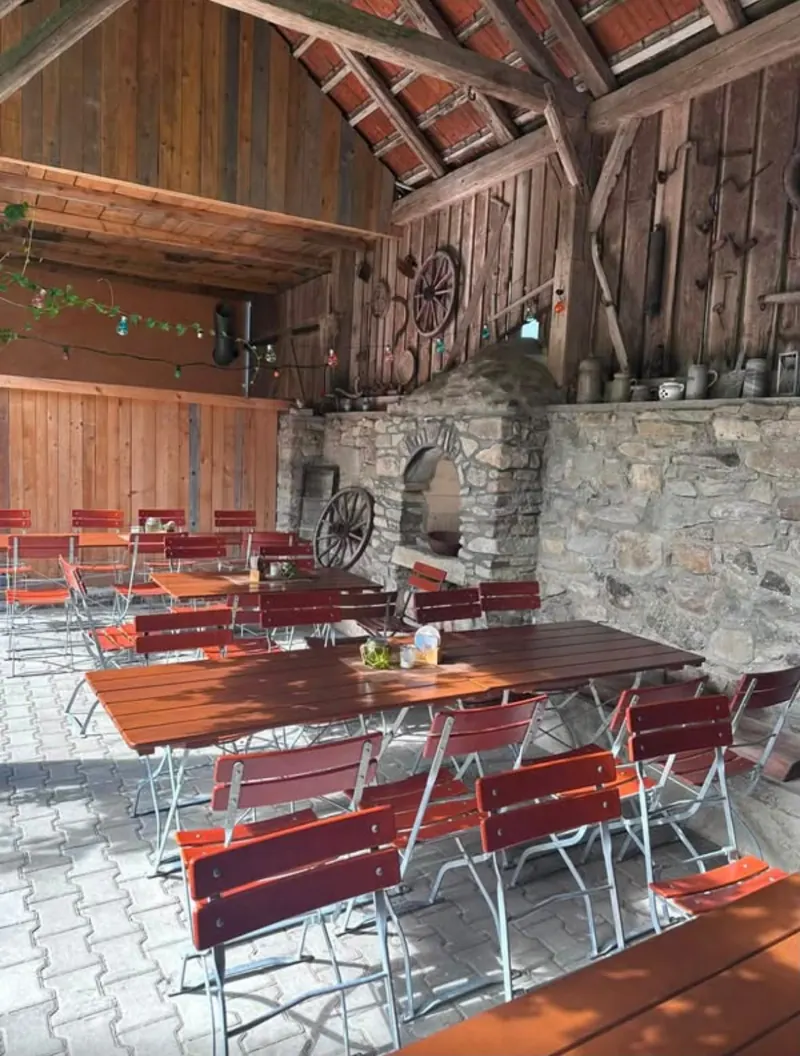 Offene Scheune mit Steinmauer, Holzgebälk und Biertischen